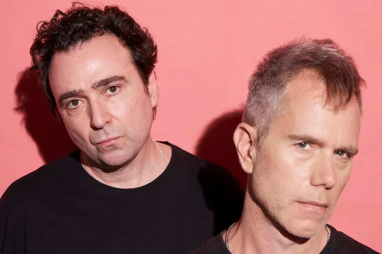Australian electronic music duo The Presets, Julian Hamilton and Kim Moyes, posing together in a press photo against a pink backdrop.